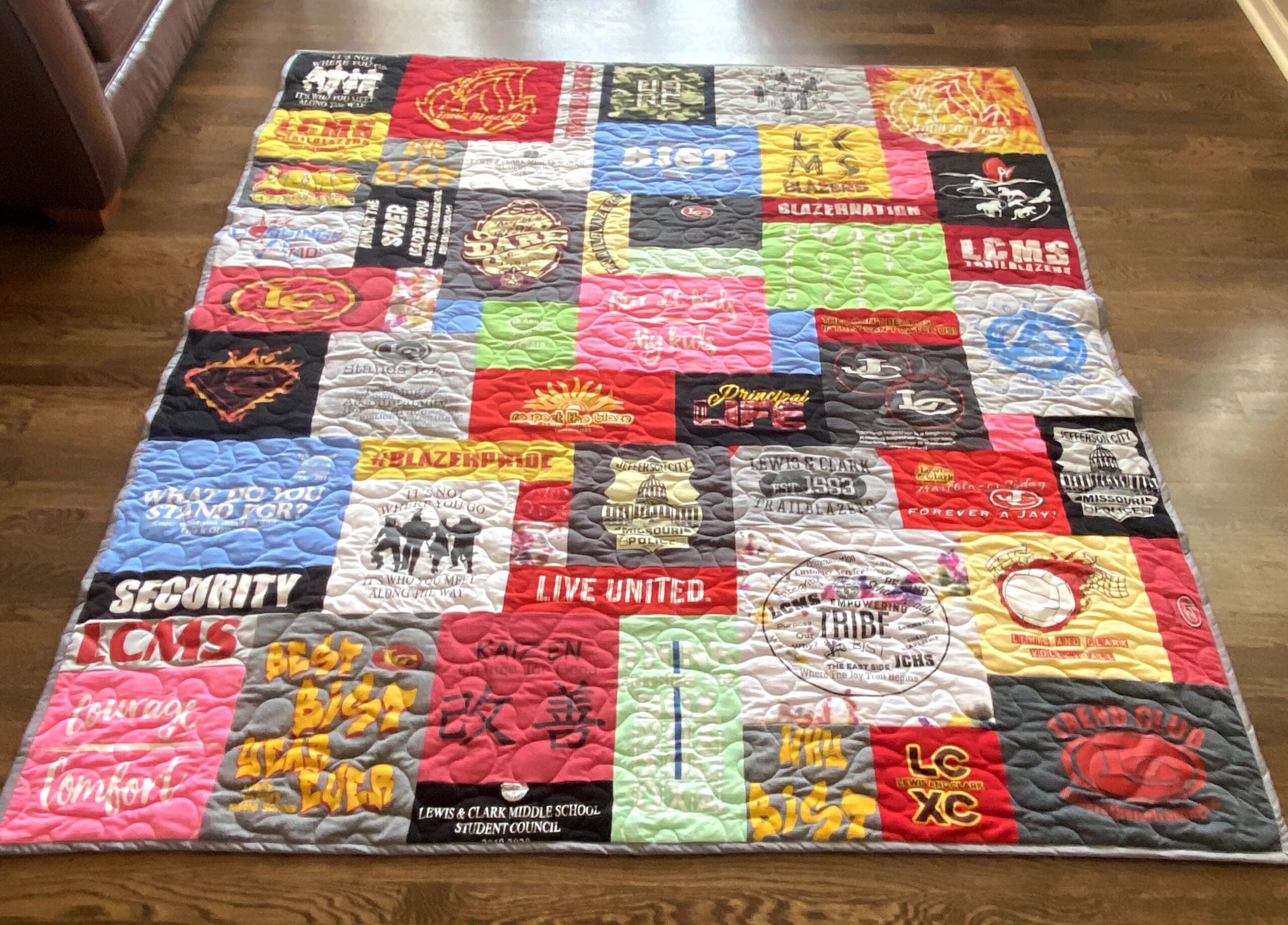 A quilt made out of t-shirts on top of a wooden floor.